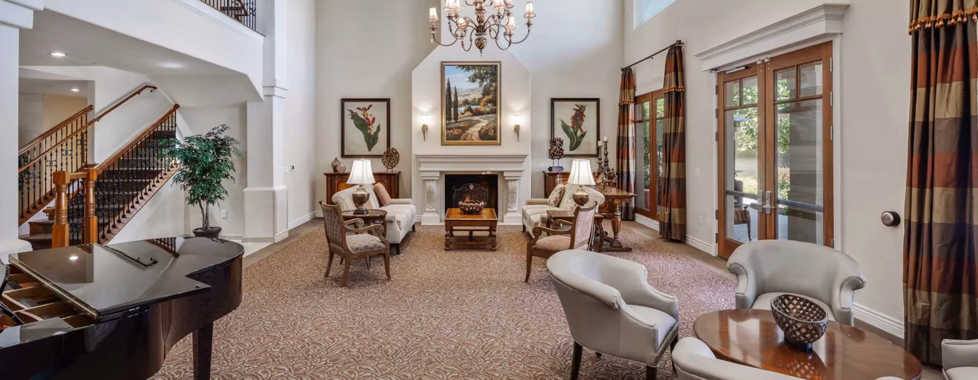 Spacious elegant lounge area with seating arranged around a fireplace, a grand piano, chandelier, and French doors.