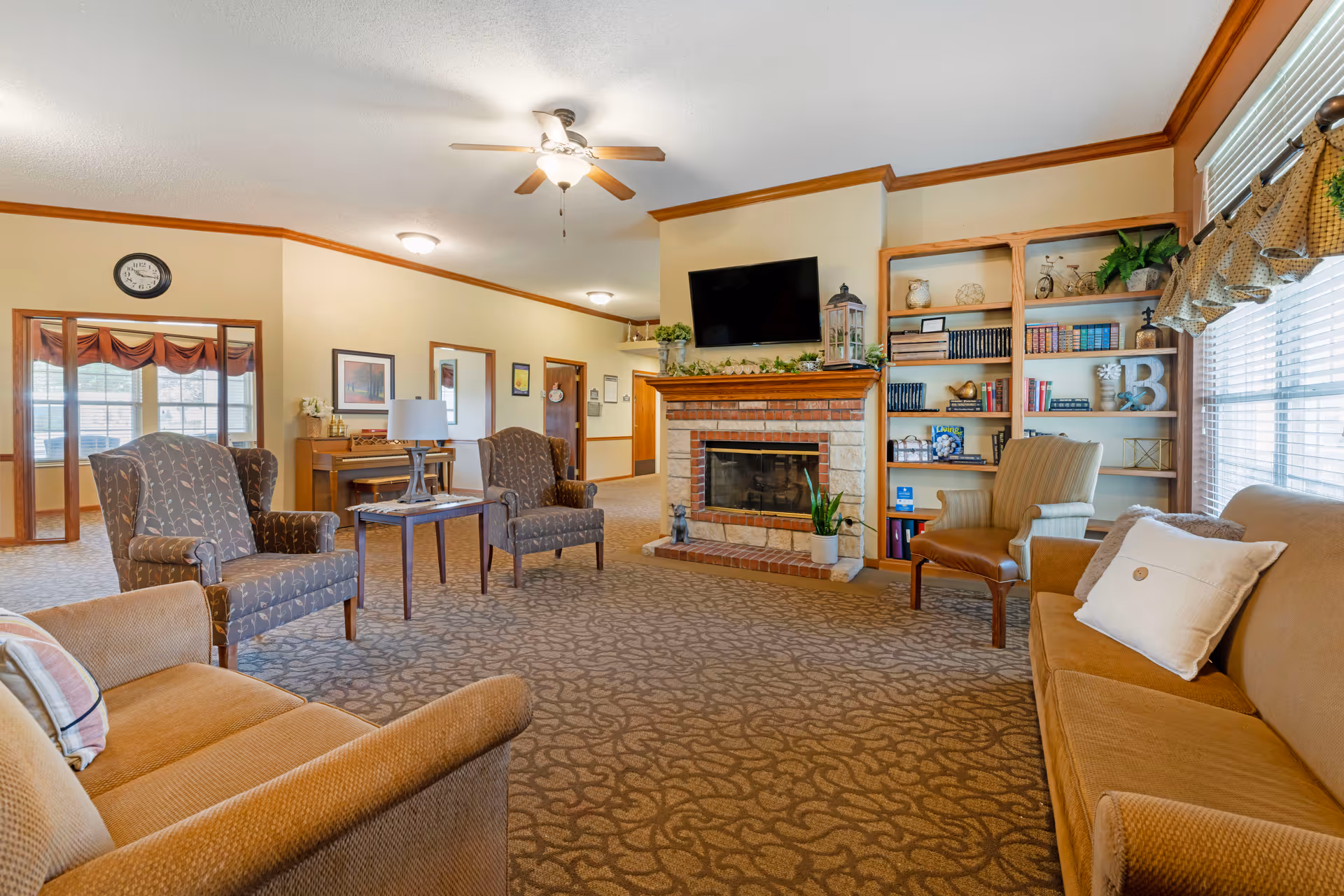 Spacious living room with sofas and armchairs arranged around a brick fireplace, built-in bookshelves, and large windows.