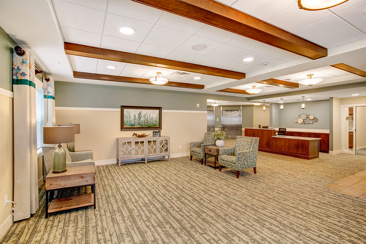 Spacious senior living lobby with seating area, reception desk, patterned carpet, and decorative ceiling beams.