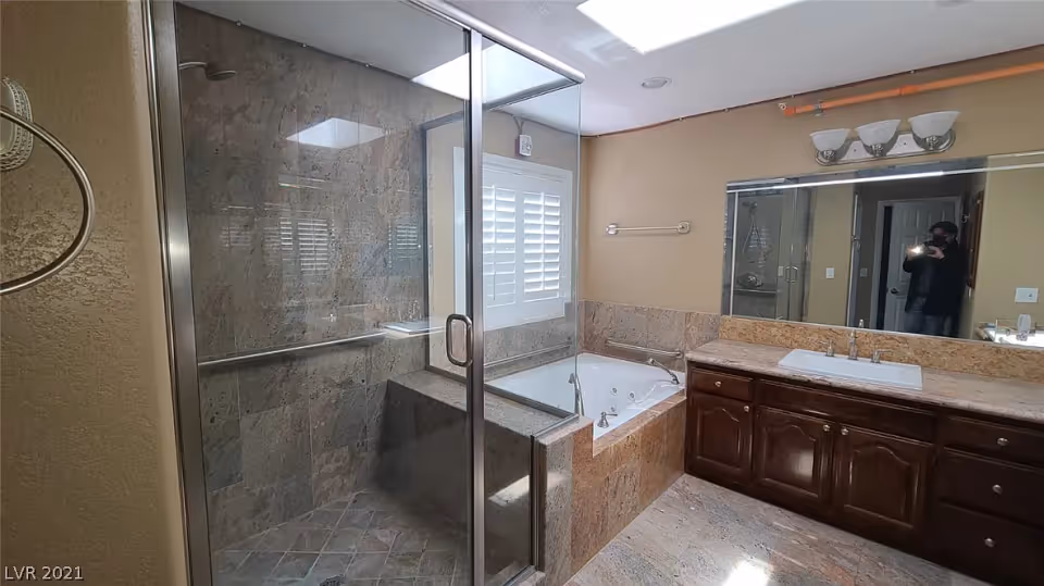 Bathroom with a glass-enclosed shower, built-in jetted tub, and a vanity with mirror and sink.