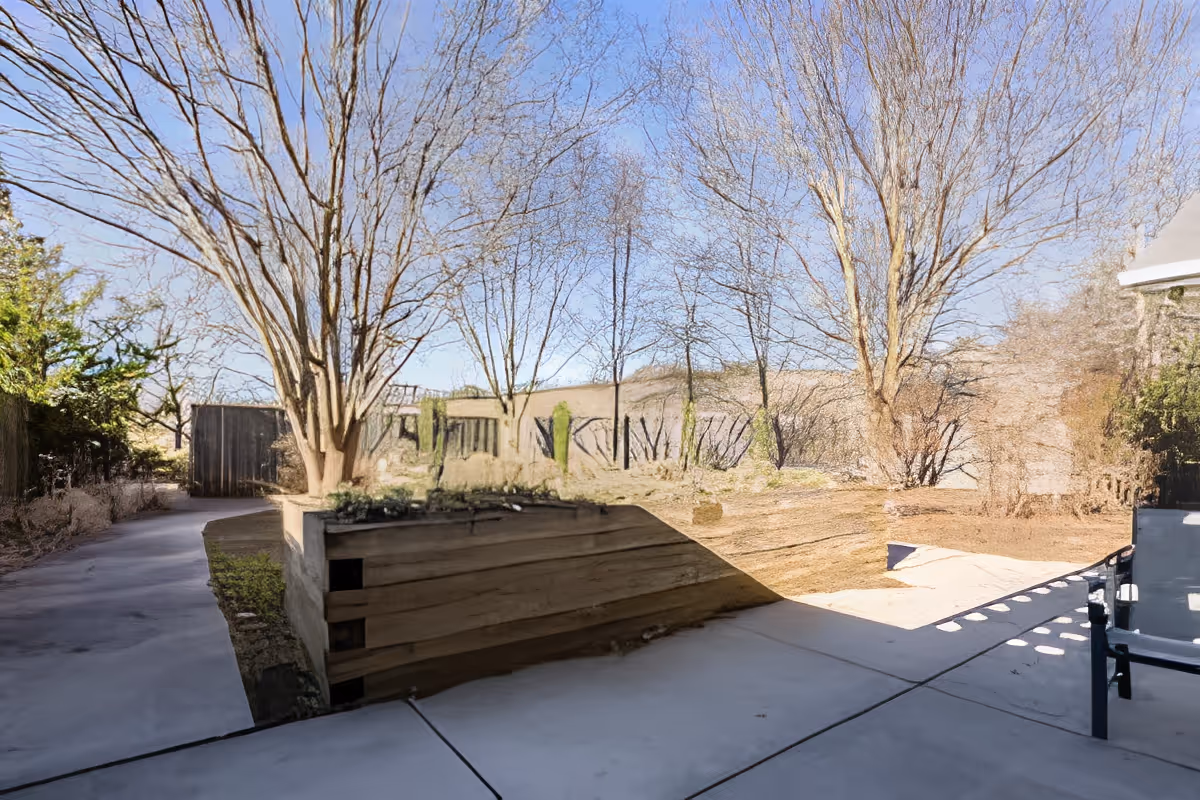 Outdoor patio and landscaped courtyard with leafless trees, a paved walkway, raised wooden planter, and patio seating.