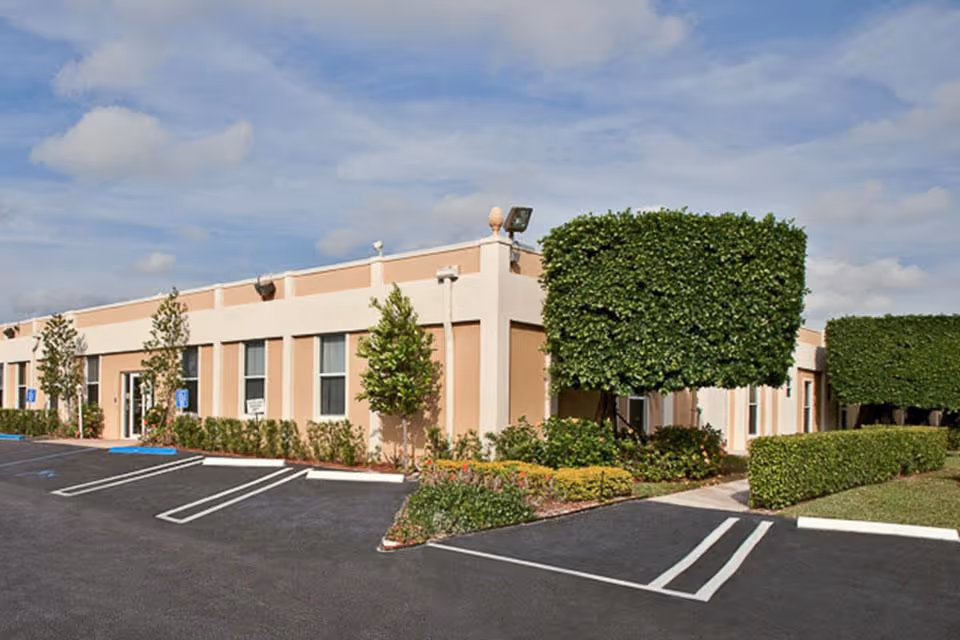 Single-story beige health center building front with trimmed hedges, landscaping, and empty parking spaces.