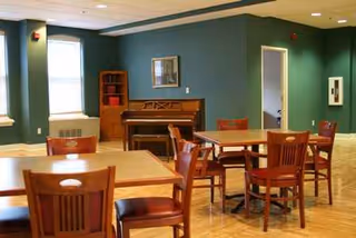 Spacious dining room with wooden tables, chairs, a piano, and teal walls.