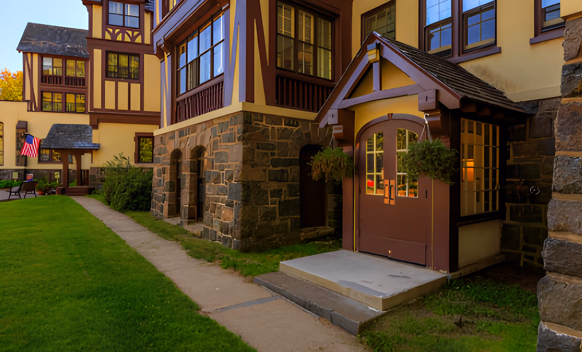 Tudor-style senior living building entrance with a small covered porch, stone foundation, walkway and green lawn.