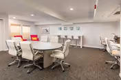 Interior common area with a large round table, white chairs, carpet, and wall art.