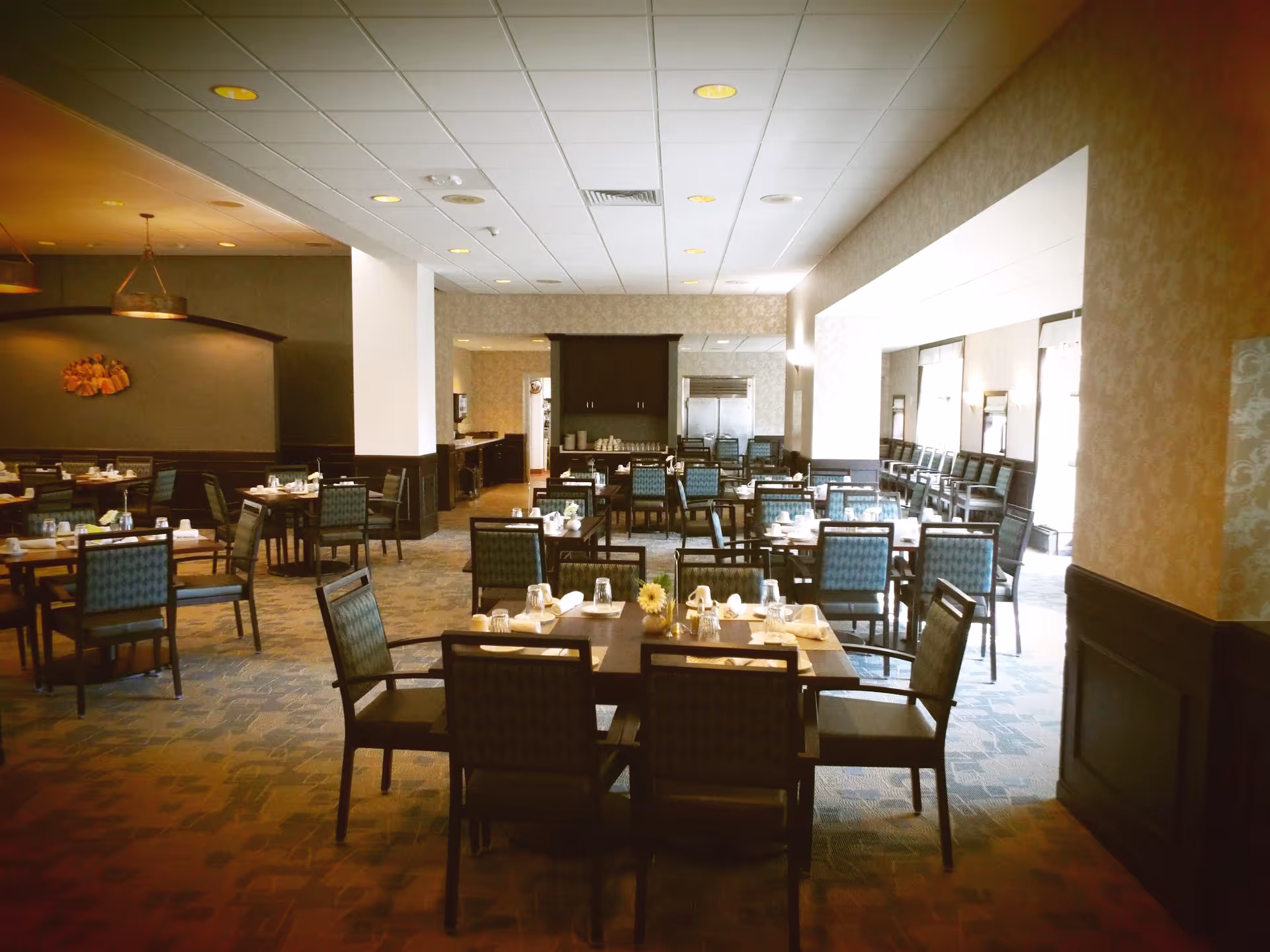 Spacious dining room with multiple set tables and chairs arranged in rows and place settings on each table.