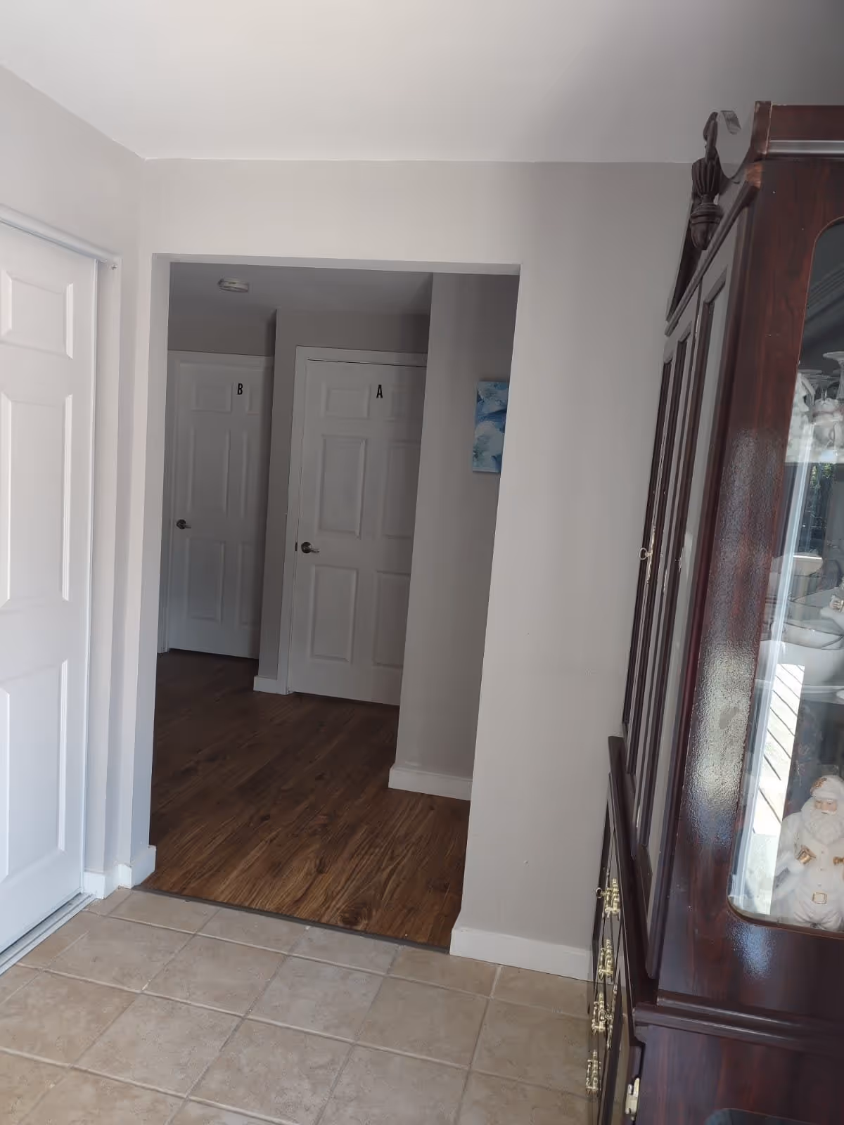 Interior hallway with tiled entry leading to wood flooring, two labeled white doors marked A and B, and a wooden display cabinet on the right.
