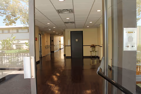 Interior hallway of Prospect Manor Assisted Living with doors, ceiling lights, and polished wooden floor.