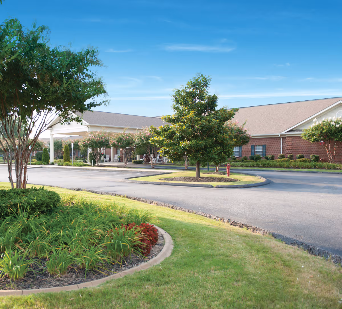 Exterior view of The Pinnacle of Southaven facility showing a circular driveway with landscaped greenery and trees under a clear blue sky.