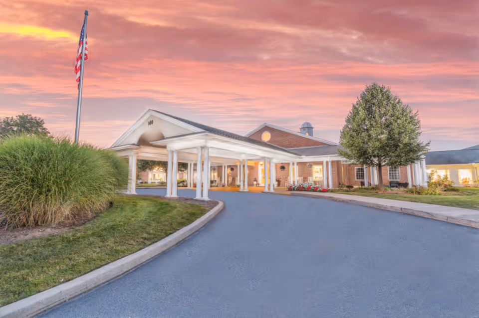 Exterior view of Heather Heights entrance with covered driveway and flag at sunset.