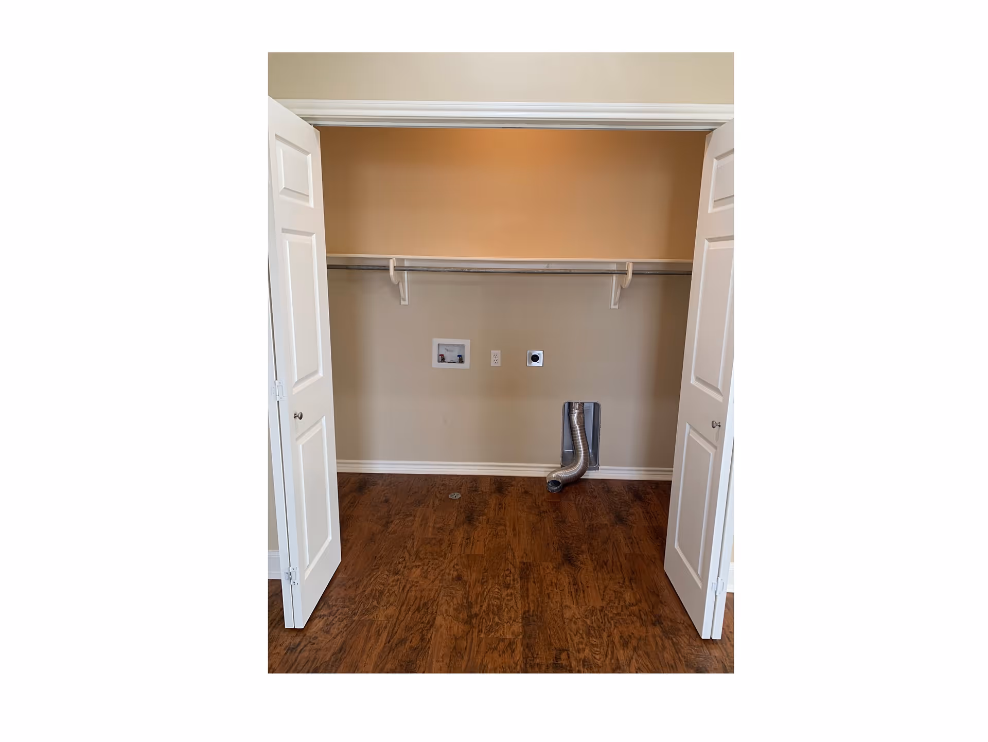 Open laundry closet with washer/dryer hookups, a shelf rod, and a flexible dryer vent hose on the floor.