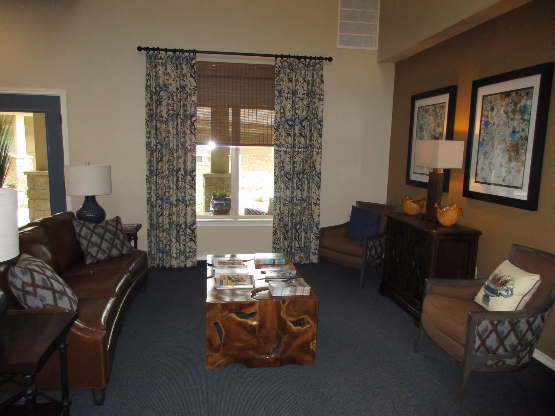 Cozy living room with a leather sofa, armchairs, a natural wood coffee table, lamps and framed artwork.