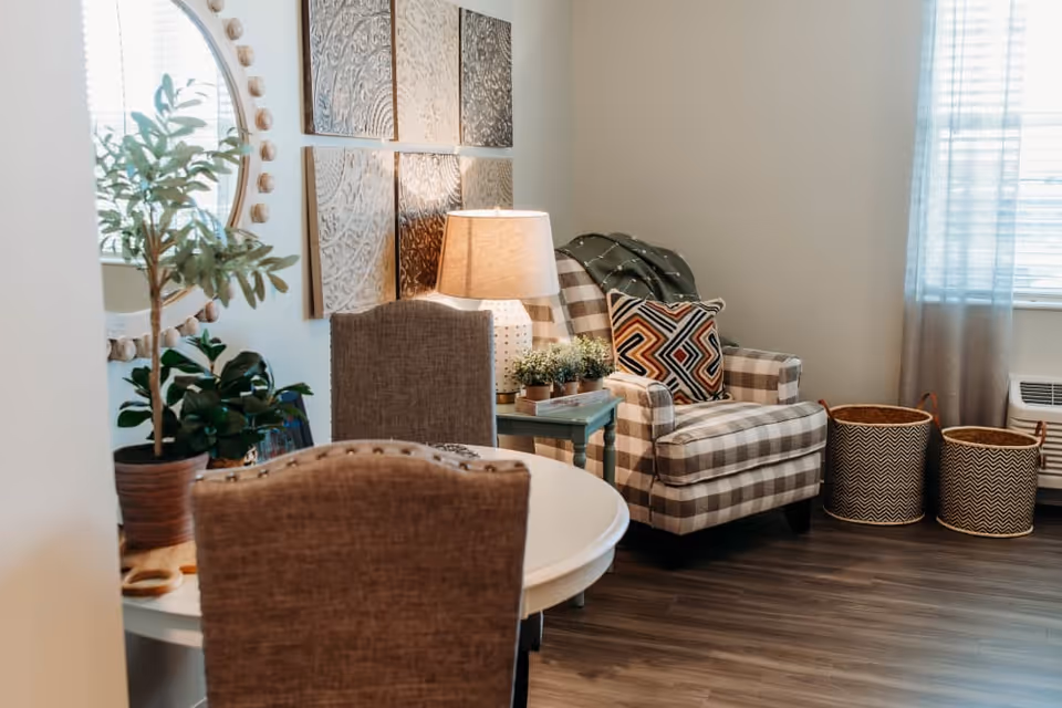 Cozy living room with a plaid armchair, side table and lamp, plants, wall art and woven baskets.