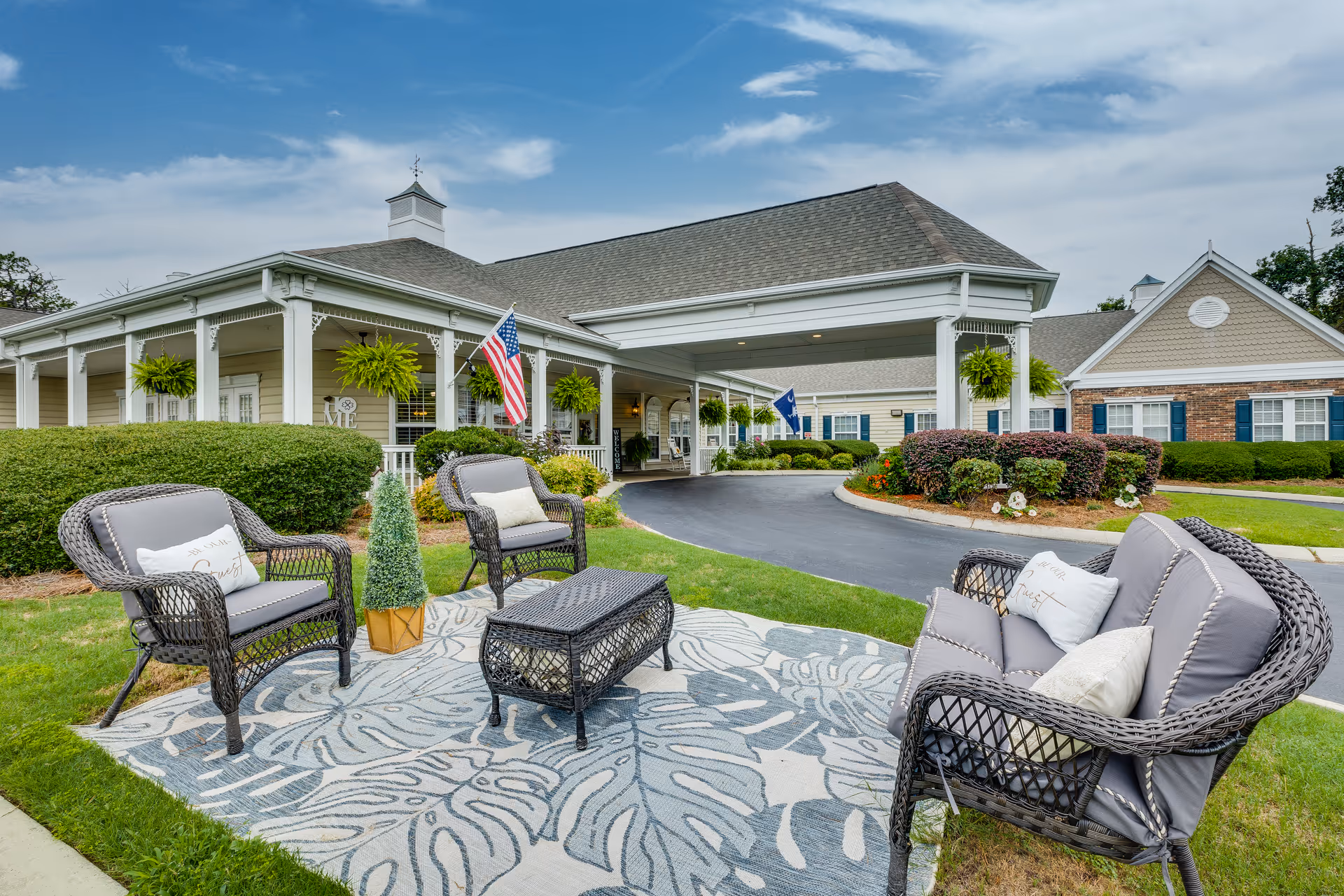 Front entrance of The Legacy of Camden senior living facility with outdoor wicker seating on a rug and a covered porte-cochère.
