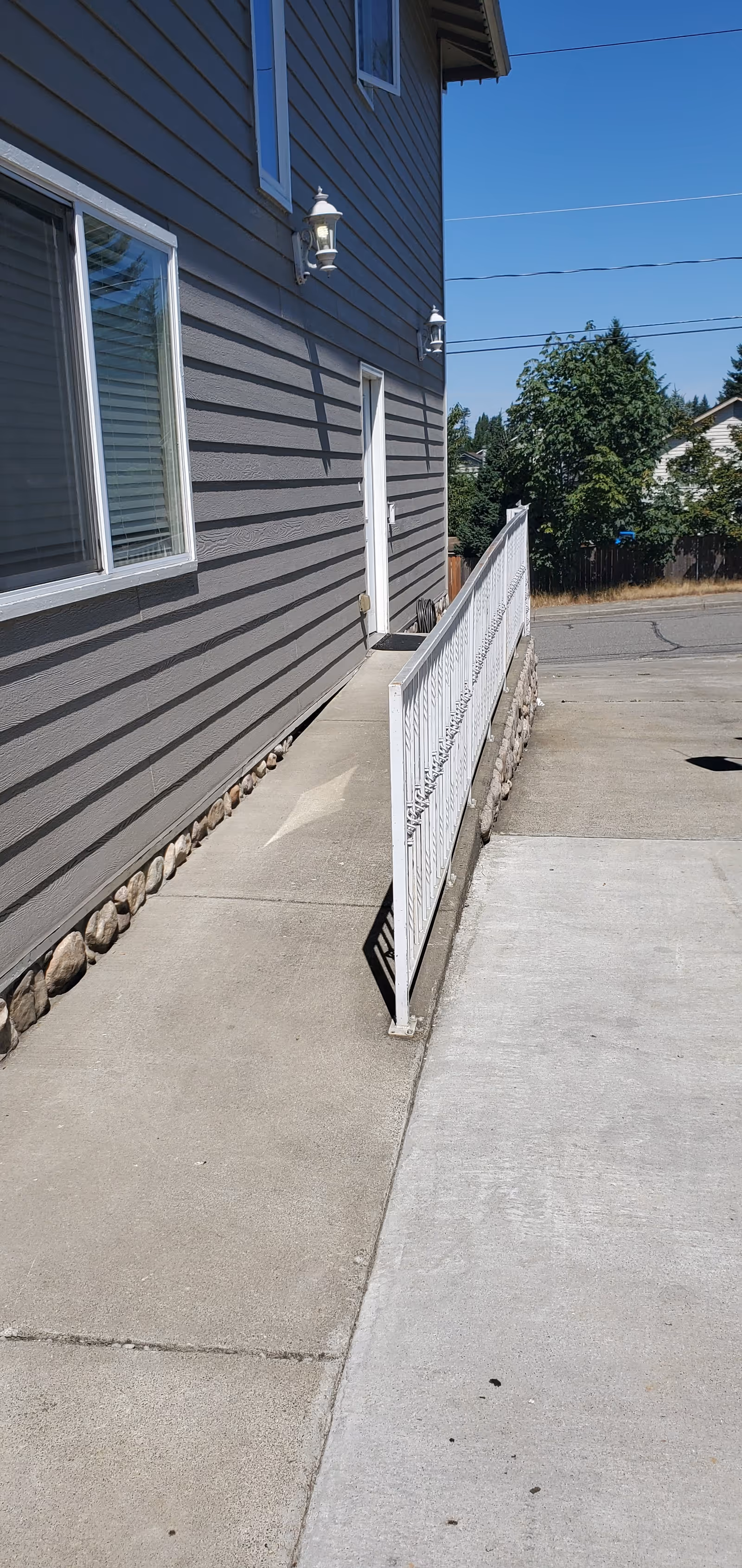 Side exterior of a gray house with a concrete ramp and white metal railing leading to a side door.