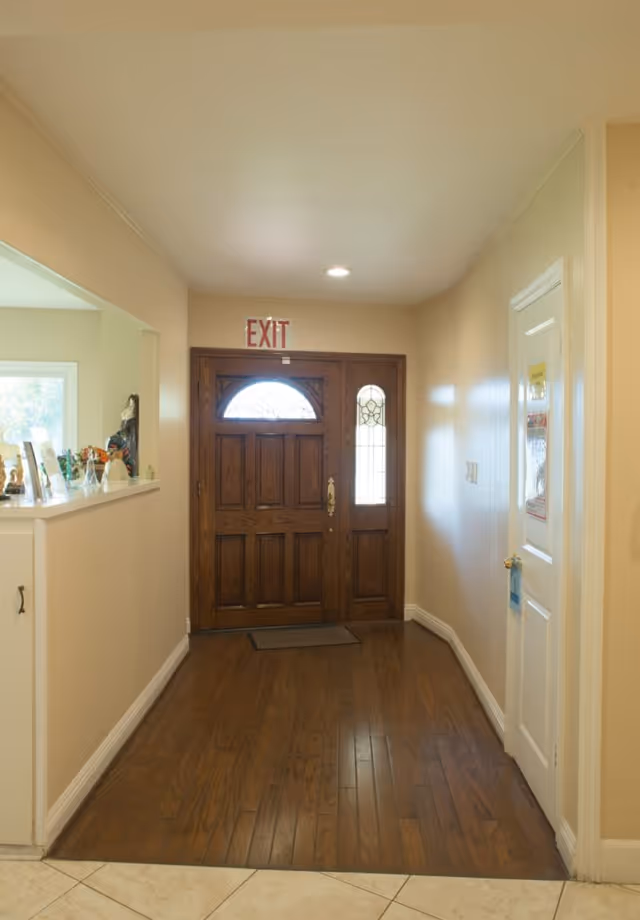 A hallway entry with a wooden front door featuring decorative glass sidelights, an EXIT sign above, and hardwood flooring.
