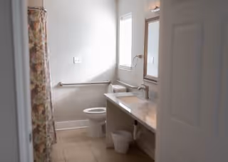 A clean bathroom with a toilet, a sink with a countertop, a mirror above the sink, a small window, a towel ring, and a floral shower curtain.