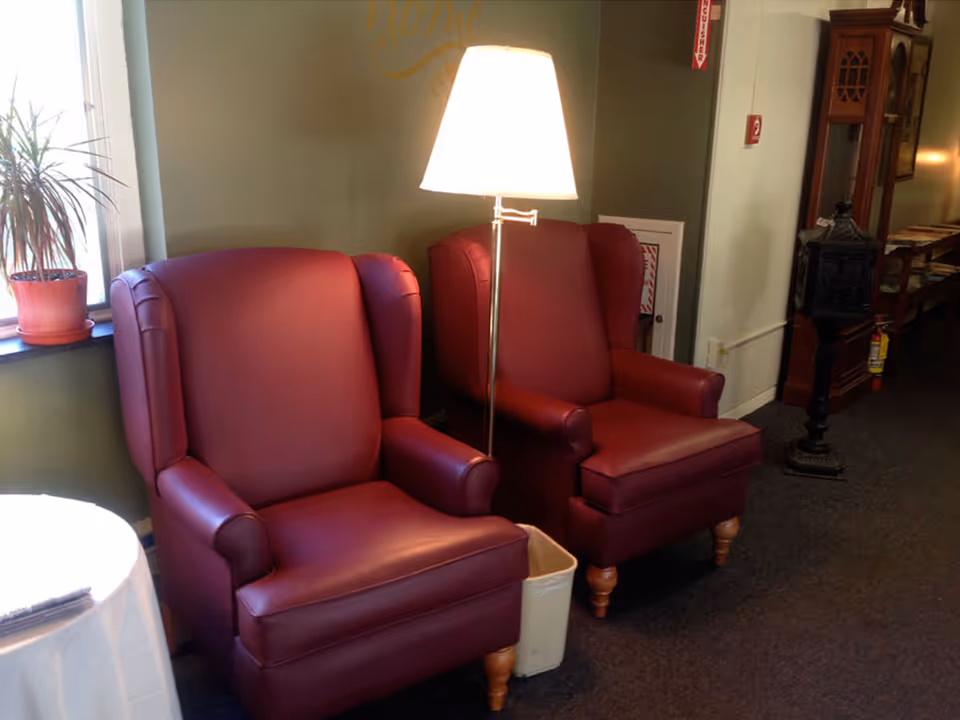 Two burgundy wingback chairs flank a lit floor lamp in a cozy sitting area.