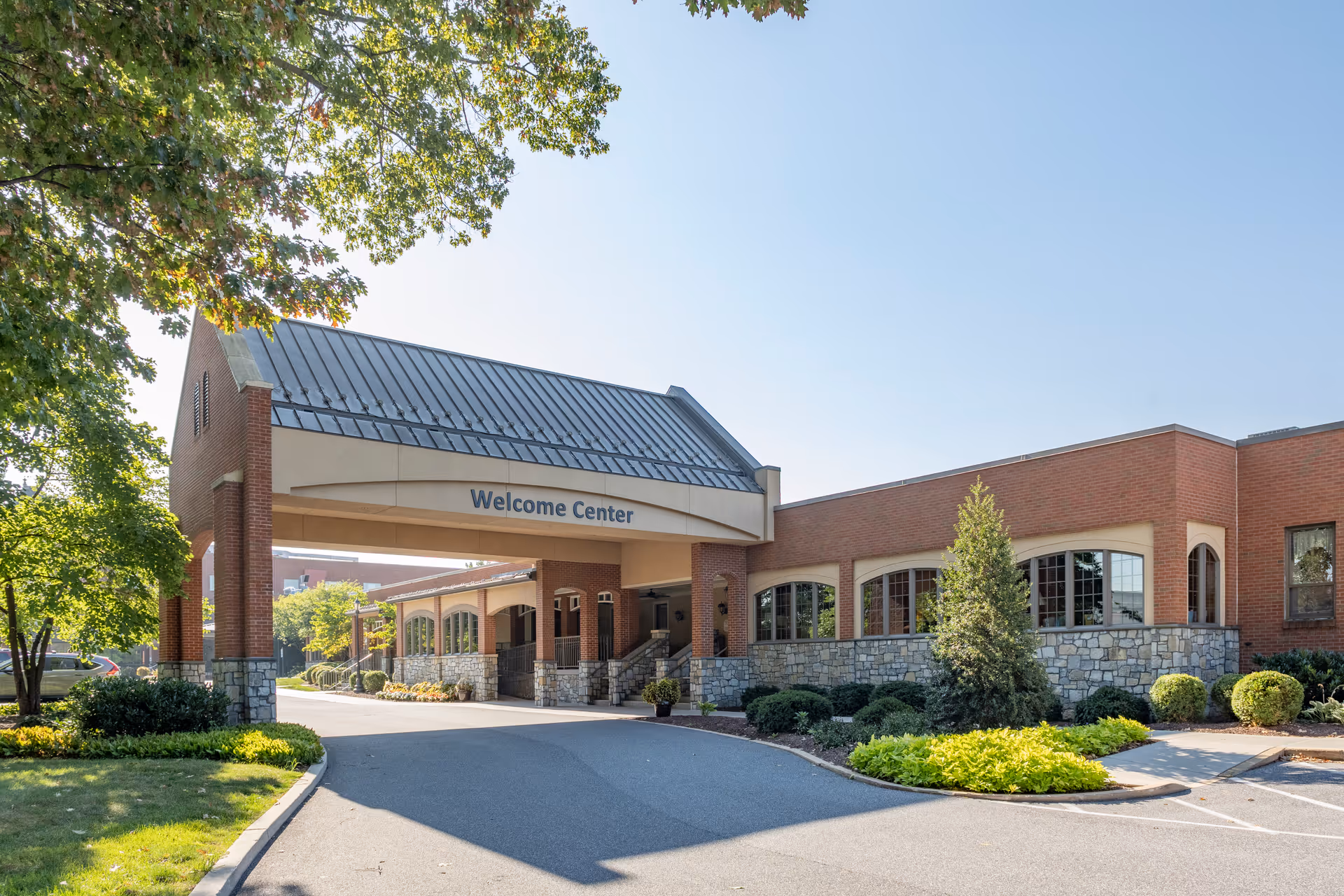 Exterior view of a building labeled Welcome Center with a covered entrance, surrounded by trees, shrubs, and a clear blue sky.