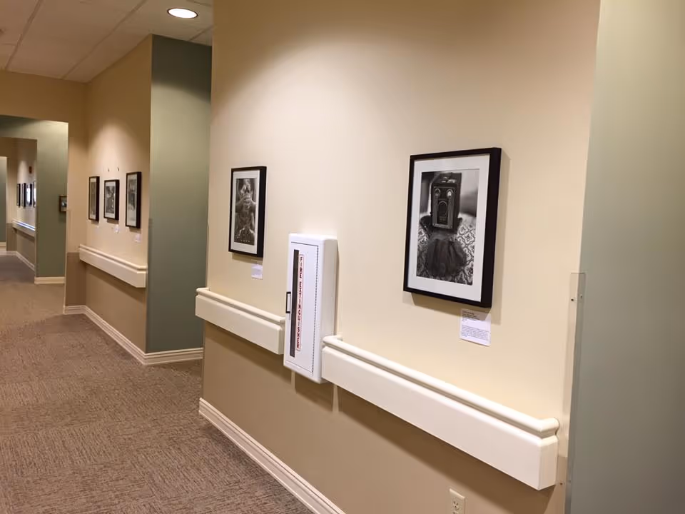 Carpeted interior hallway with handrails, framed black-and-white photographs on the walls and a recessed fire safety cabinet.