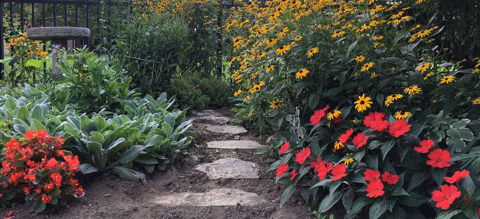 Stone stepping-stone path through a garden bordered by yellow and red flowering plants and lush greenery.