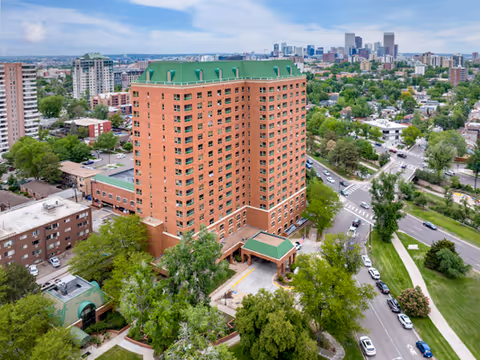 Aerial view of a tall brick senior living building with a green roof in a city.