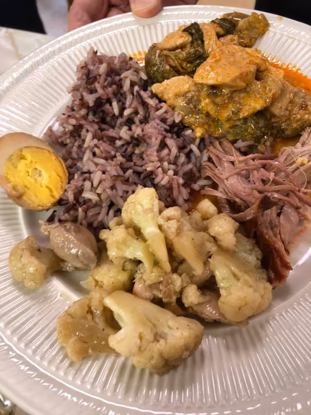 Paper plate with purple rice, cauliflower, shredded meat, a halved boiled egg, and a saucy meat and vegetable stew.