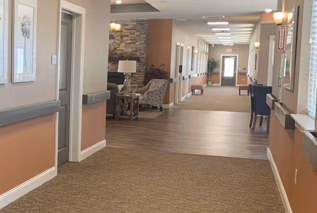 Well-lit interior corridor of a retirement facility with seating alcoves, wall art, and a distant exit door.