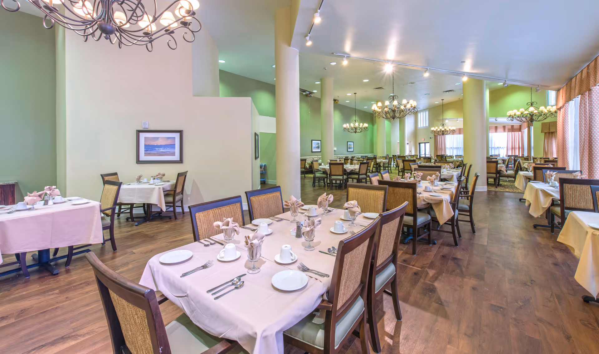 Spacious dining room with multiple set tables, chandeliers, and wood flooring.