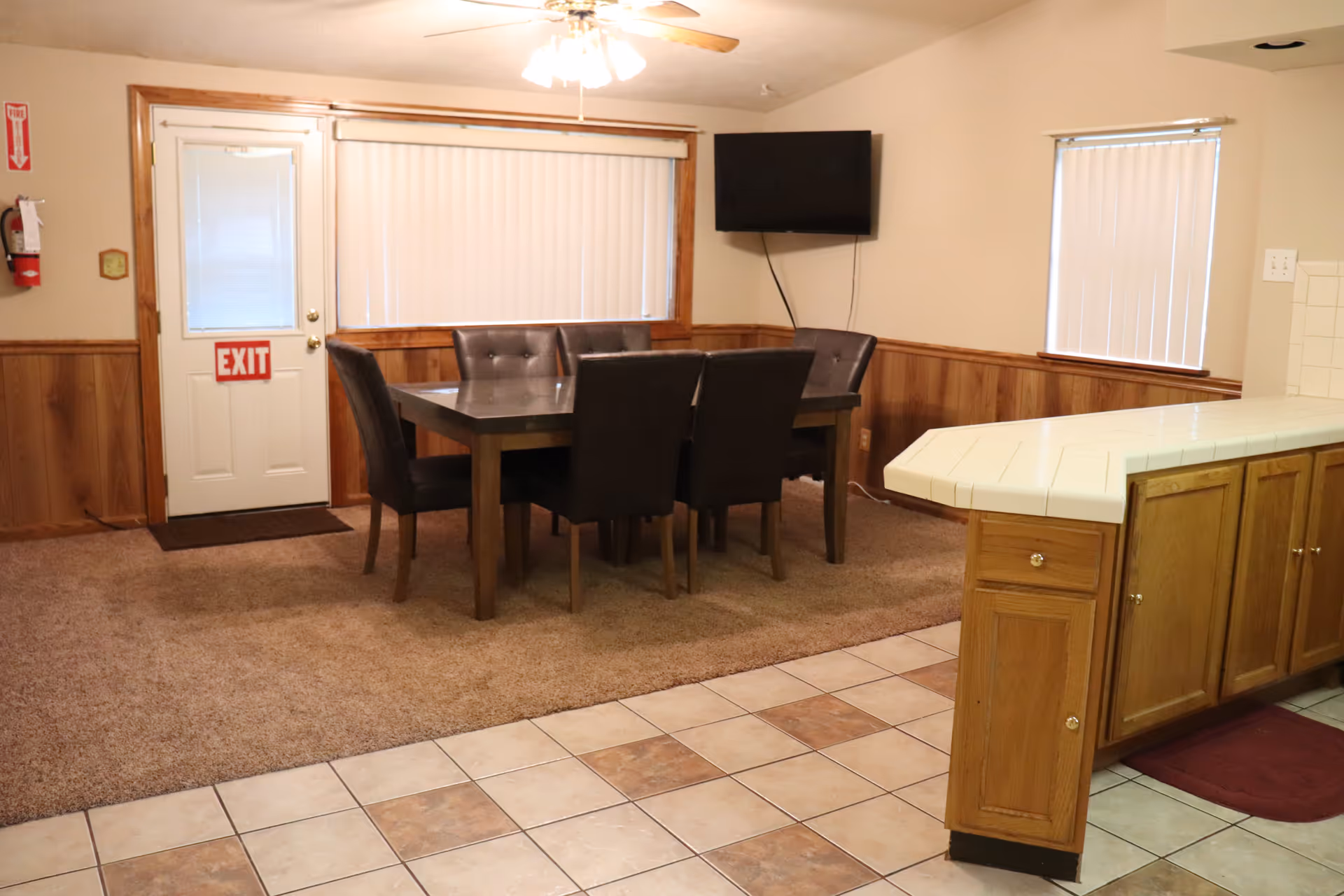 Dining area with a table and six chairs next to a tiled kitchen counter and an exit door.