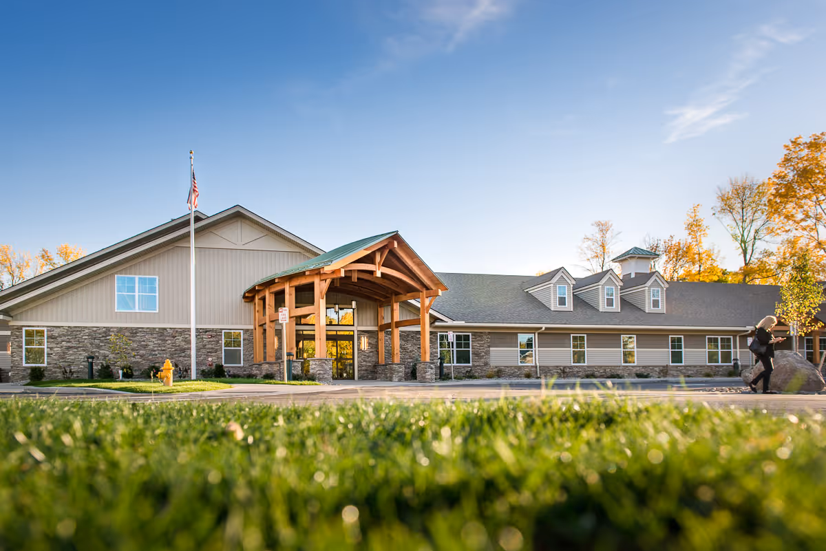Front exterior of the Legacy at Maiden Park building with a covered wooden entrance, flagpole, and a grassy foreground.