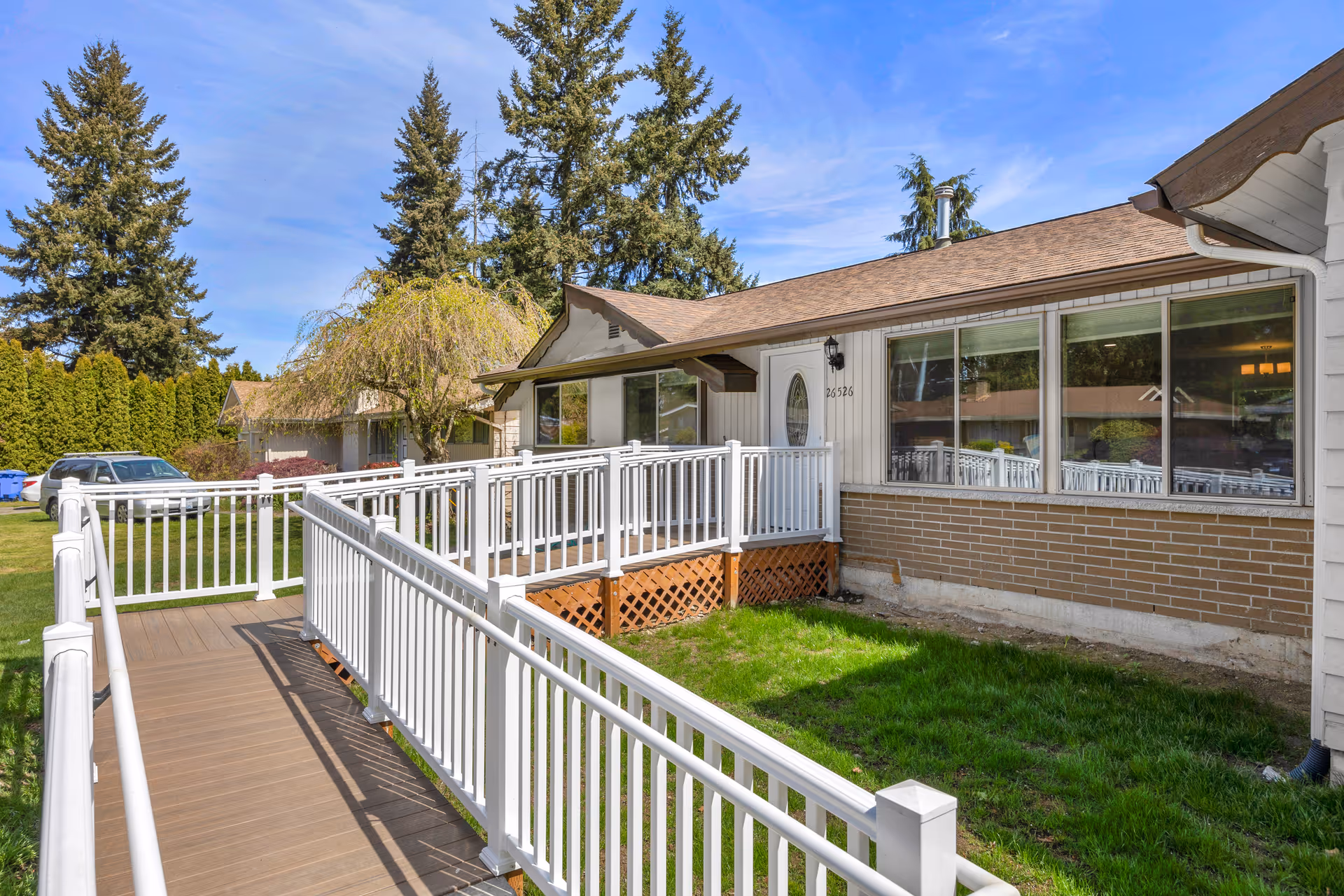 Single-story home's front exterior with a white-railed wheelchair ramp leading to the entrance and lawn.