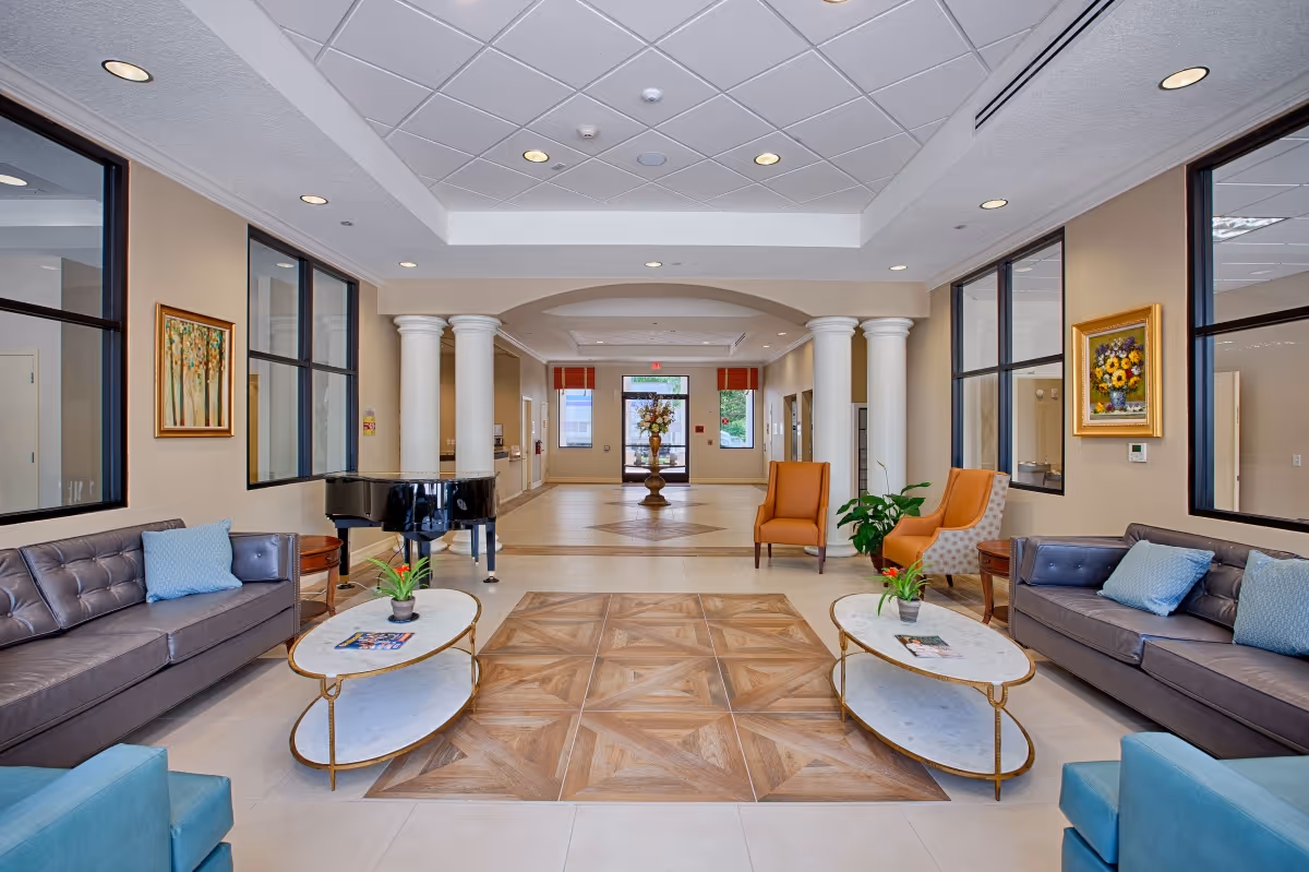 Spacious senior living lobby with sofas, armchairs, coffee tables, a grand piano and columns leading to the entrance.