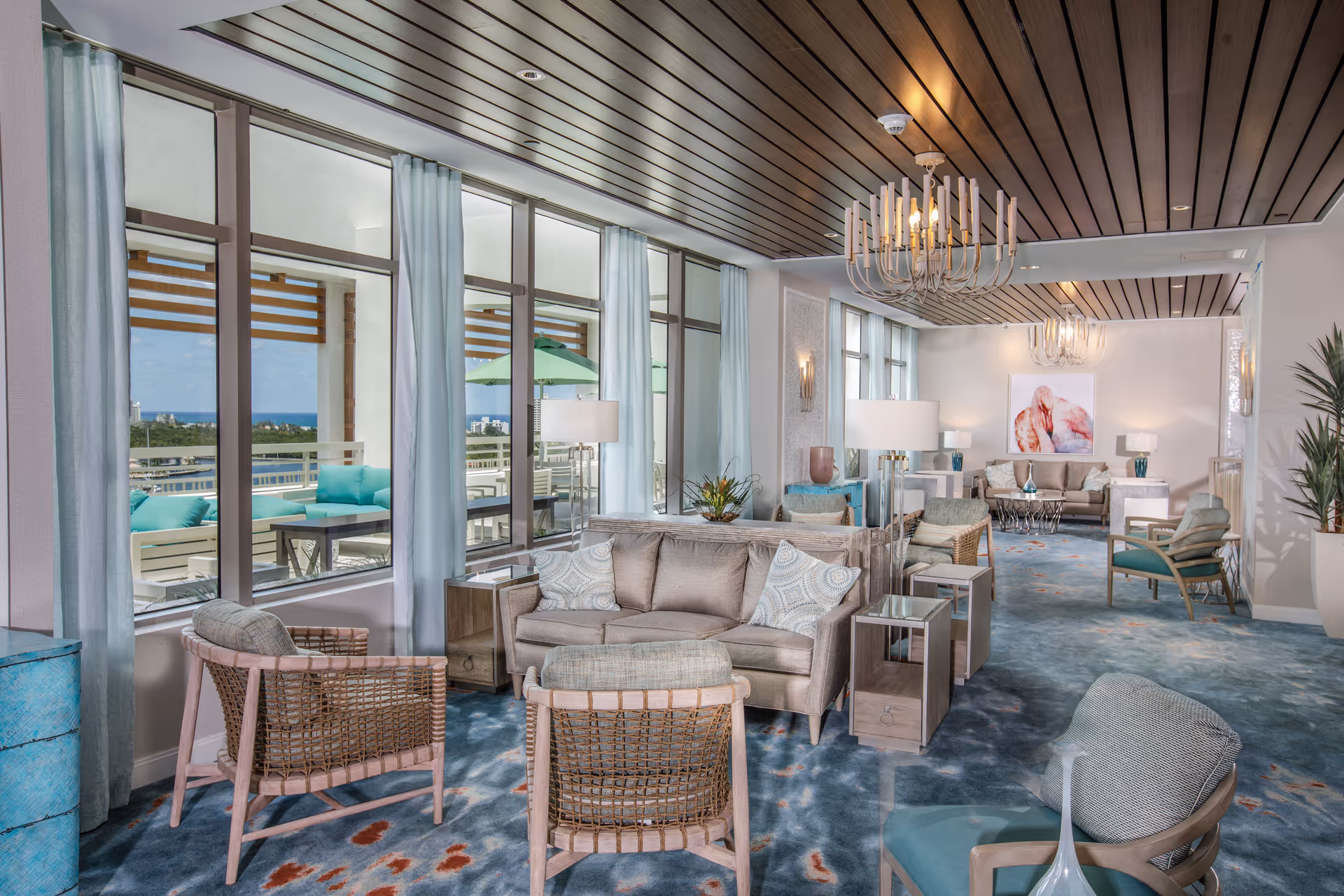 Bright upscale communal lounge with sofas, armchairs, chandeliers and large windows looking out onto a terrace.