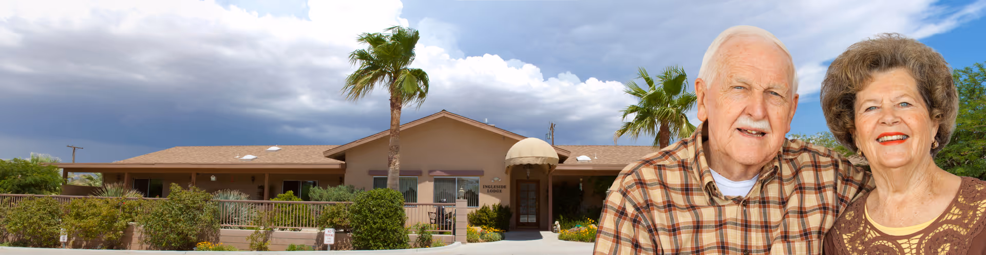 Exterior front view of Ingleside Lodge Assisted Living facility with a clear sky and two palm trees in front. An elderly man and woman are smiling in the foreground on the right side of the image.