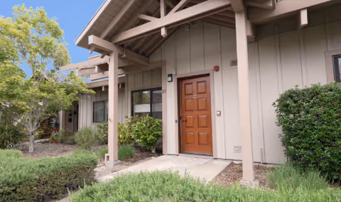 The entrance of a senior living facility with a wooden door and landscaped surroundings.