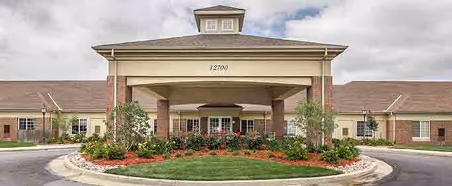Front exterior view of Antioch Valley Senior Living facility featuring a large covered entrance with columns, a circular driveway, landscaped greenery, and a partly cloudy sky.