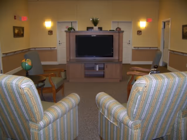 Common living area with upholstered armchairs arranged facing a television in a wooden entertainment cabinet.