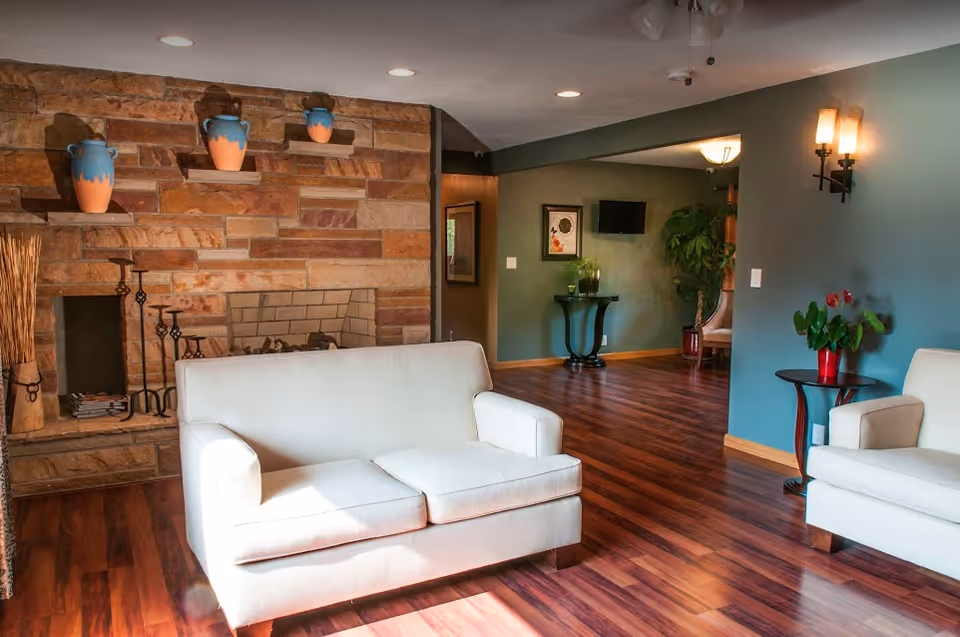Bright living room with two white sofas, hardwood floors, a stone fireplace with decorative vases, and green-painted walls.