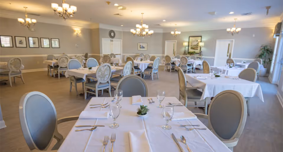 Bright formal dining room with round-backed chairs and tables set with white tablecloths and place settings.