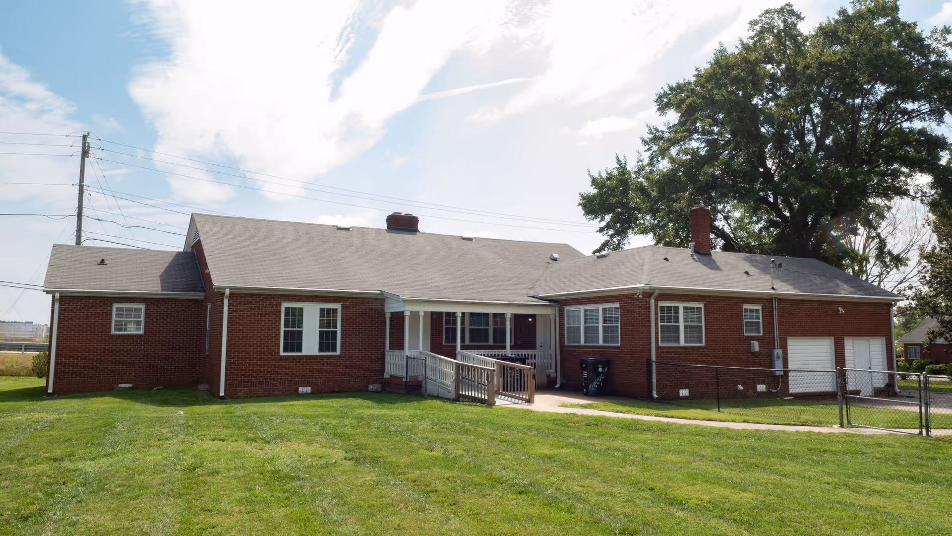 A single-story brick senior care home with a lawn, ramp, and front entrance.