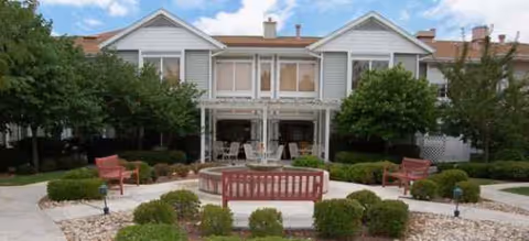 Two-story senior living facility's front exterior with a central fountain and surrounding seating.