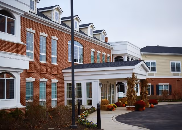 A brick senior living facility exterior with a covered entrance and fall decorations.
