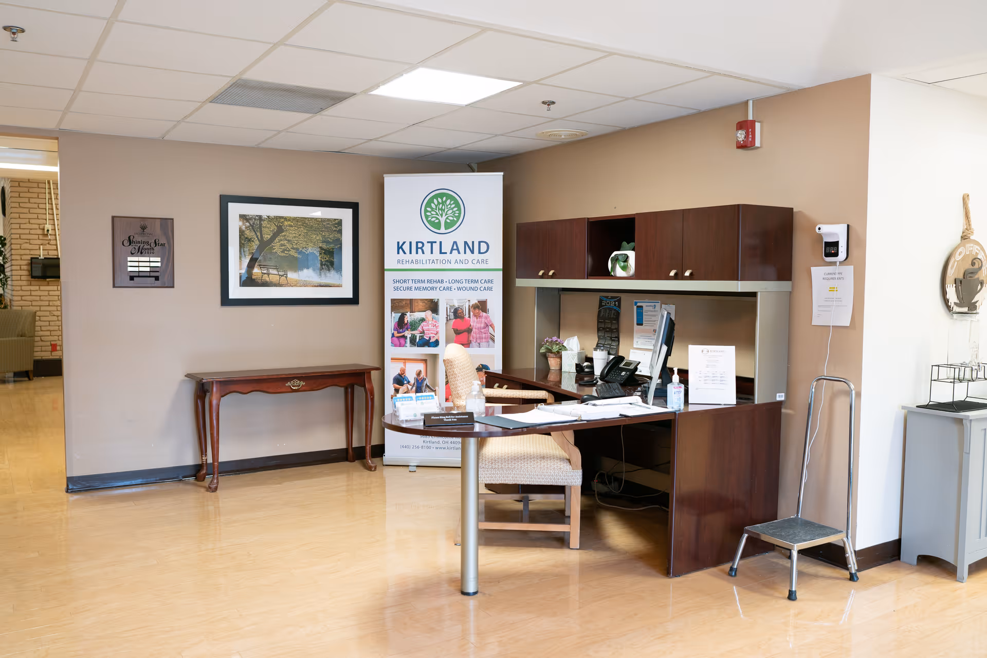 Reception desk and seating area with a Kirtland banner, framed art, and a small table in a facility lobby.