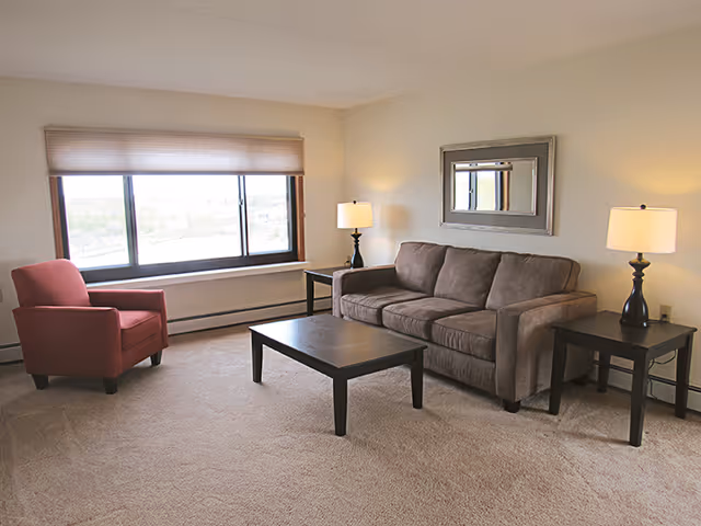 Living room with a gray three-seat sofa, red armchair, coffee table, side tables with lamps, a wall mirror, and a large window.