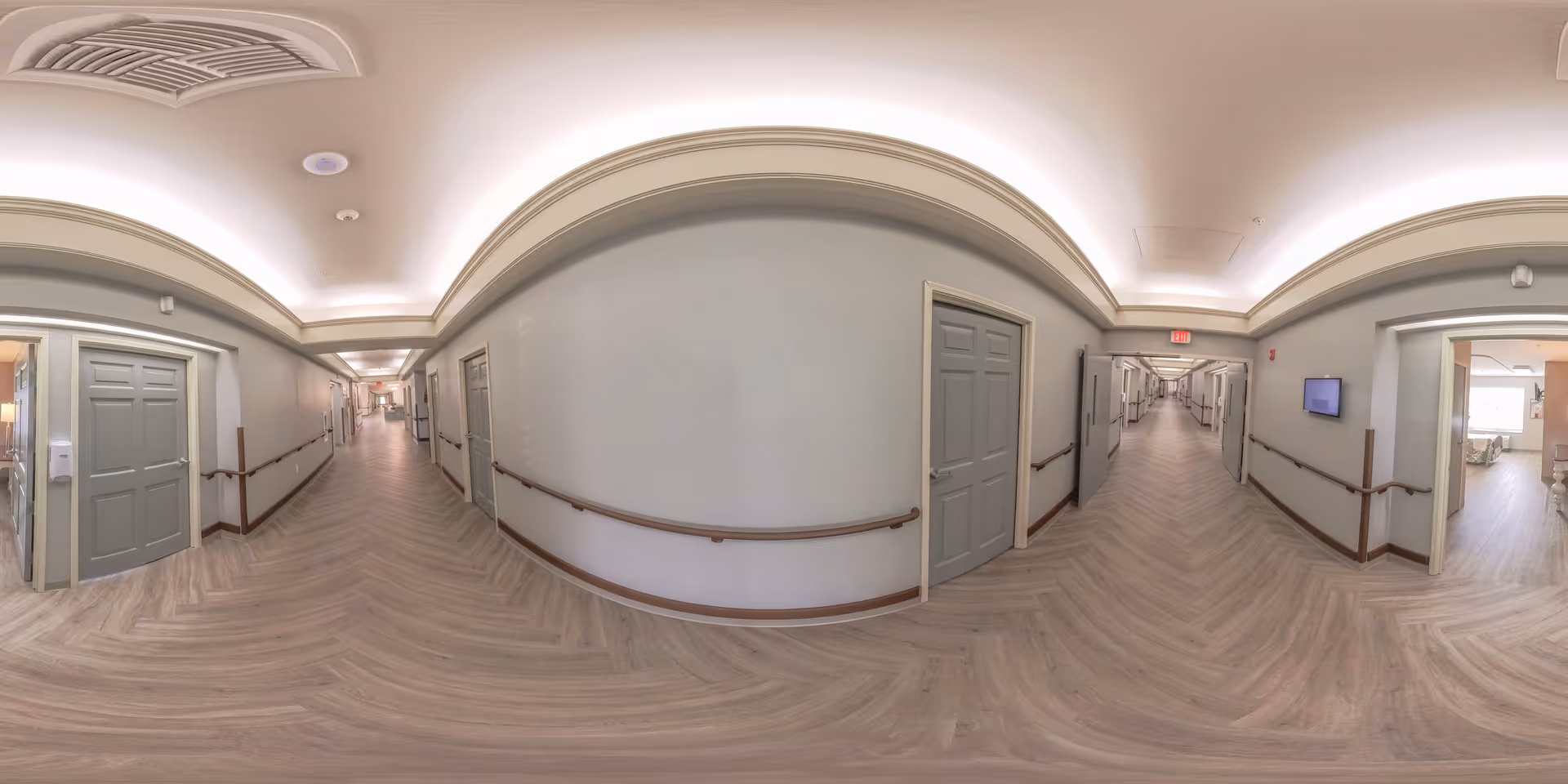Interior hallway of a senior living facility with wood-look floors, handrails, doors on both sides, and recessed ceiling lighting.