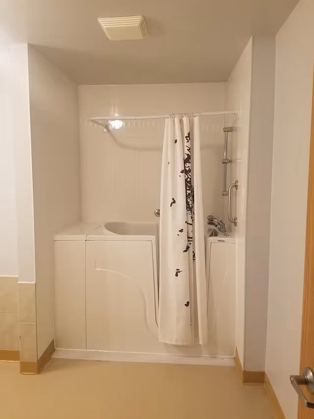 Walk-in bathtub/shower with a white patterned shower curtain, grab bar, and tiled walls in a bathroom.