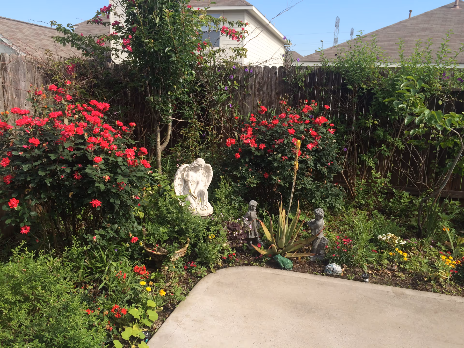 Outdoor garden with colorful flowers, statues, and a curved concrete pathway.