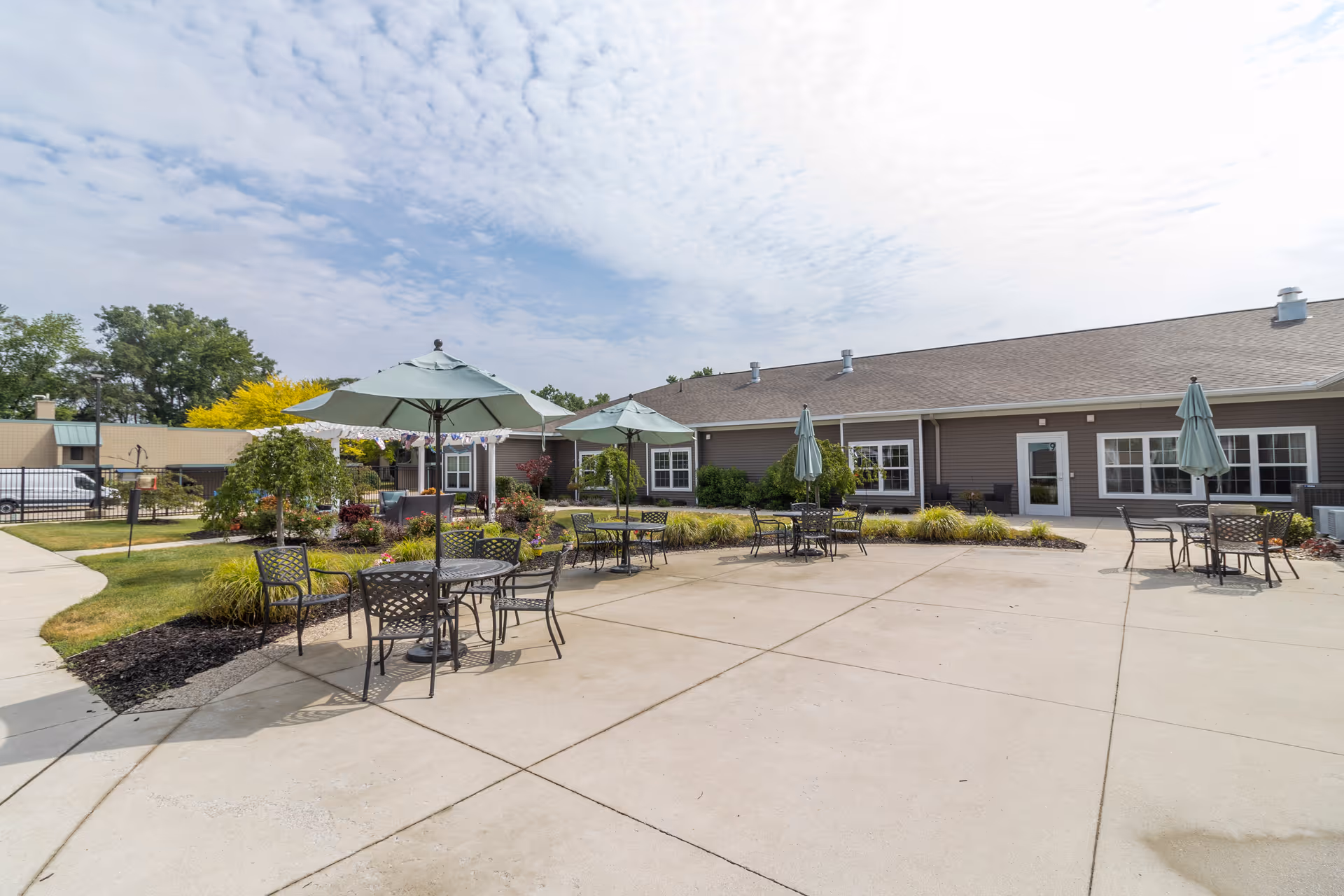 Outdoor patio courtyard with metal tables, chairs, and umbrellas beside a single-story building.