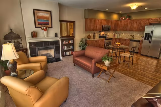 Open-plan living room with armchairs, a loveseat, fireplace, and an adjacent kitchen and dining area with stainless steel appliances.